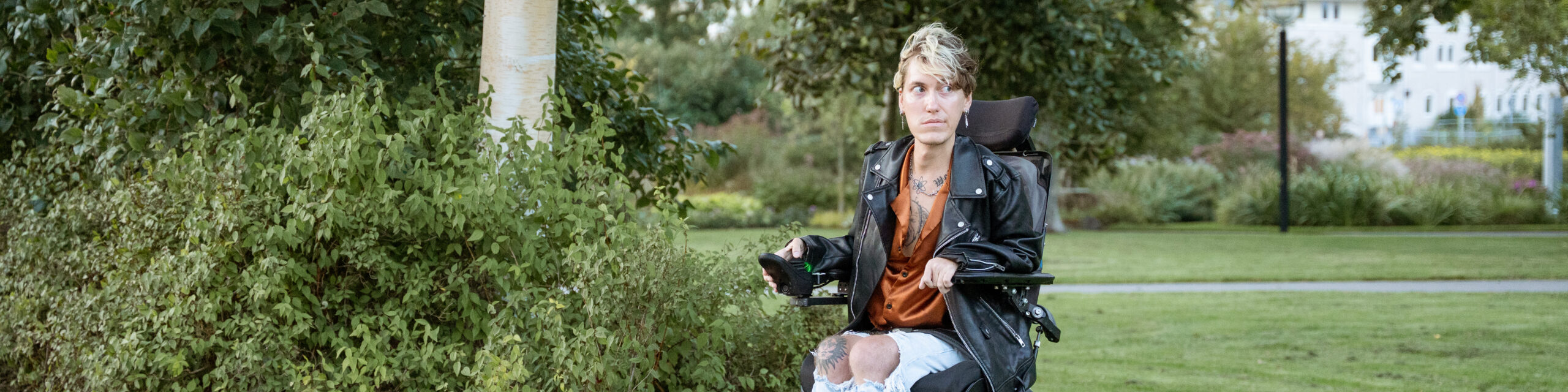 En man i el-rullstor framför ett buskage i en park